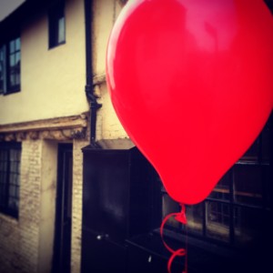 A red balloon floats down an old side street