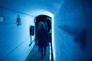 People walking through a corridor underneath Tower Bridge, bathed in blue light